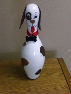 a white and brown dog figurine sitting on top of a wooden table next to a wall