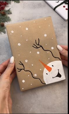 a hand holding a brown box with a snowman painted on it and trees in the background