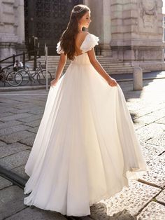 a woman in a white wedding dress standing on the street with her back to the camera