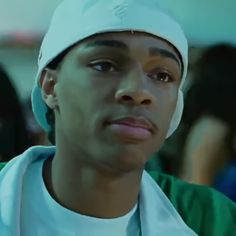 a young man wearing a white hat and green shirt looking at the camera with other people in the background