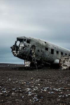 an old airplane sitting on top of a field next to rocks and grass with the sky in the background