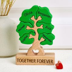 a wooden tree with two names on it and a heart in the center, sitting next to a vase