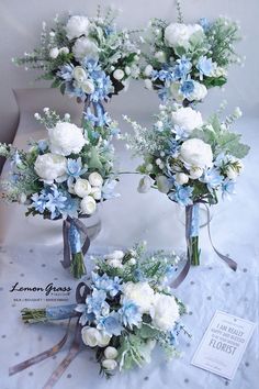 three bouquets of white and blue flowers are arranged on a table with silver ribbon