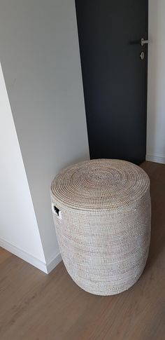 a large white basket sitting on top of a wooden floor next to a black door