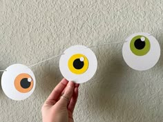 someone is holding up some paper balls with eyes on them hanging from a line in front of a wall