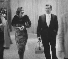 black and white photograph of two people walking down a hall with other people in the background