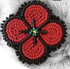 a close up of a red and black beaded brooch on a white fur