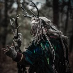 a man dressed in native american clothing with horns and feathers on his head, holding an animal's antlers