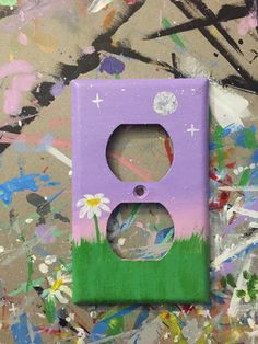 a purple and green light switch cover sitting on top of a wall covered in paint