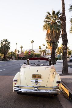 an old car is parked on the side of the road in front of palm trees