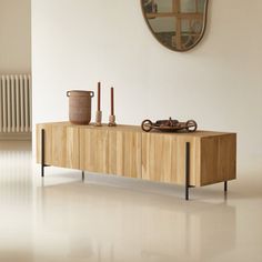 a large mirror hanging on the wall above a wooden cabinet in a room with white walls