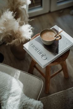 a cup of coffee sitting on top of a table next to a book and chair