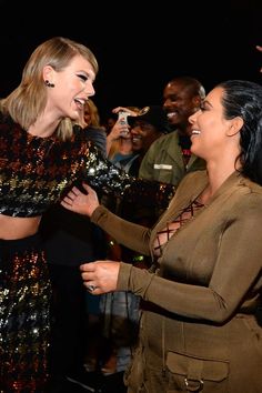 two women laugh as they stand in front of a group of people at an event