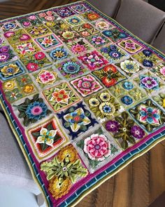 a table topped with a colorful blanket covered in crocheted flowers and leaves on top of a wooden table