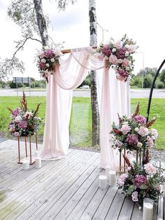 an outdoor ceremony setup with pink and white flowers on the altar, candles and drapes