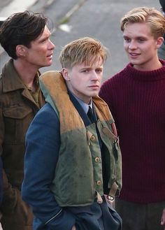 three young men standing next to each other in front of a street with one man looking at the camera