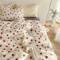 an unmade bed with red hearts on it and white sheets in the middle, next to a small side table