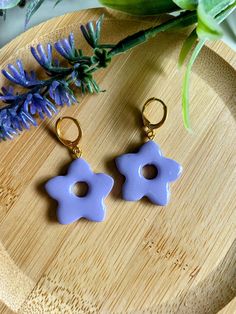 two blue flower shaped earrings sitting on top of a wooden tray next to purple flowers