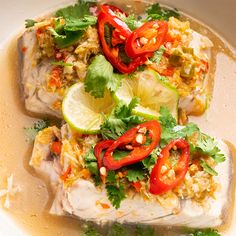 two fish fillets covered with vegetables and garnishes in a white bowl