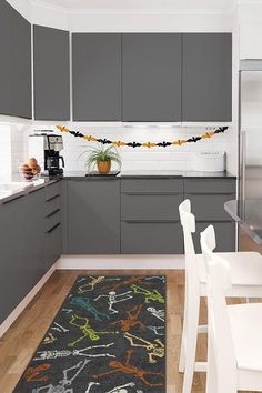 a kitchen with gray cabinets, white chairs and an area rug in the middle of the floor