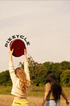 two girls are playing with a frisbee in a field, one girl is reaching up to the sky