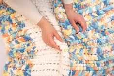 a woman is holding onto a multicolored crocheted blanket with her hands