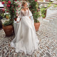 a woman in a wedding dress standing next to some potted plants and pink flowers