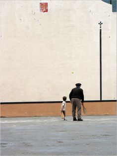 a man and child standing in front of a building with a ball on the ground