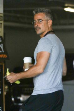 a man with glasses holding a cup and an apple in his hand while standing next to a sign