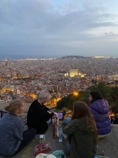 three women sitting on top of a hill overlooking a city at night with lights in the distance