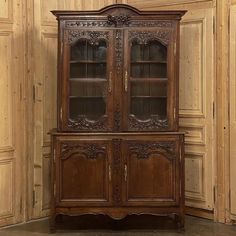 an old wooden china cabinet with glass doors and carvings on the front, against a wood paneled wall