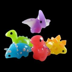 four different colored plastic toys in the shape of dinosaurs on a black background, with one toy shaped like a fish