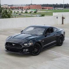 a black mustang parked in a parking lot next to a wall and grass covered field