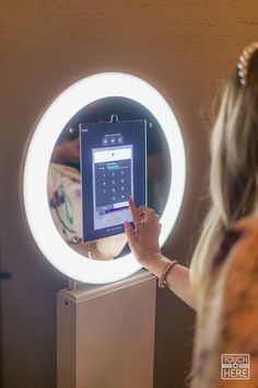 a woman standing in front of a mirror looking at her cell phone and pointing to the screen