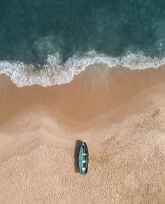 an aerial view of a boat on the beach with waves coming in from the ocean