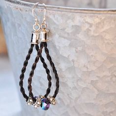 two black braided leather earrings with silver bells hanging from them on a potted plant