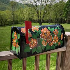 a painted mailbox sitting on top of a wooden fence next to a lush green field