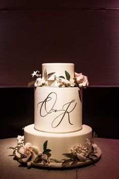 a three tiered cake with white flowers on the top and initials on the side