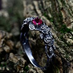 a silver ring with a red stone in the middle sitting on a tree branch,