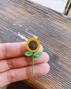 a hand holding a paper flower on top of a wooden table