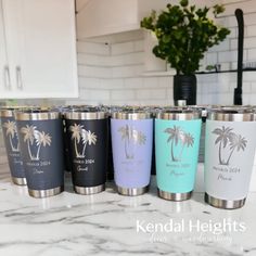 six travel mugs are lined up on the counter in front of a potted plant