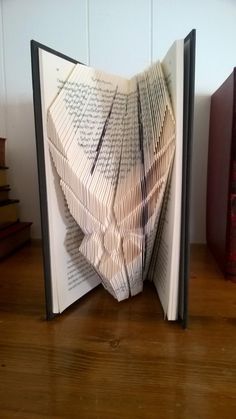 an open book with folded pages sitting on top of a wooden table