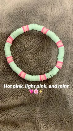 a bracelet with pink and green strips on it, sitting on a gray blanket that says hot