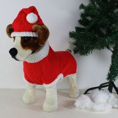 a stuffed dog wearing a sweater and hat next to a christmas tree with snow on the ground