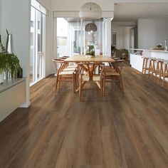 a dining room with wood flooring and table in front of an open kitchen area