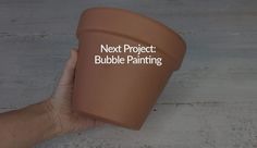 a hand holding a clay cup with the words next project bubble painting written on it