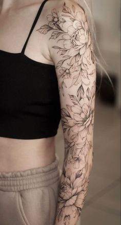 a woman's arm with flowers on it and a black bra top in the background