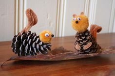 two stuffed animals made out of pine cones sitting on top of a wooden table next to each other