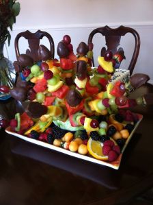 a tray full of fruit sitting on top of a wooden table next to a vase filled with flowers