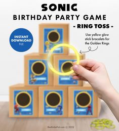 a hand holding a ring tosser in front of a stack of cardboard boxes with the words sonic birthday party game on it